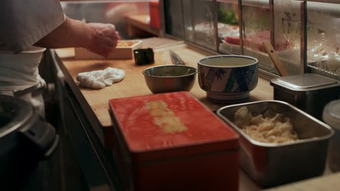 Professional sushi chef making sea urchin Maki and placing it in front of two customers in small sushi bar with soft interior lighting. Close up shot on 4k RED camera.: film stockowy