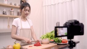 Blogger Asian woman using camera recording how to make salad healthy food video for her subscriber, female use organic vegetables preparing salad for fit body at home.