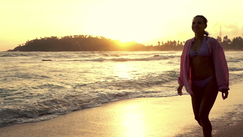 Young woman walking on the beach during sunset, super slow motion
