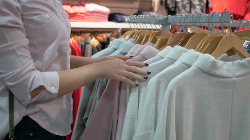 Fashion shopping, female hands are choosing stylish new clothes on hangers in store close-up during seasonal discounts and trying on myself | Shutterstock HD Video #1020030475