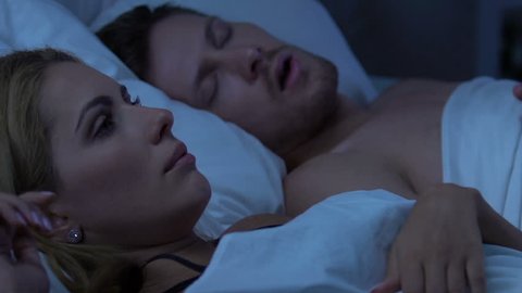 Couple sleeping in bed, displeased wife awakened by loud snore of husband