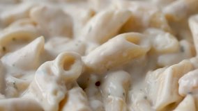 Very close video of pasta and chicken in an alfredo sauce steaming and cooking in a pan.