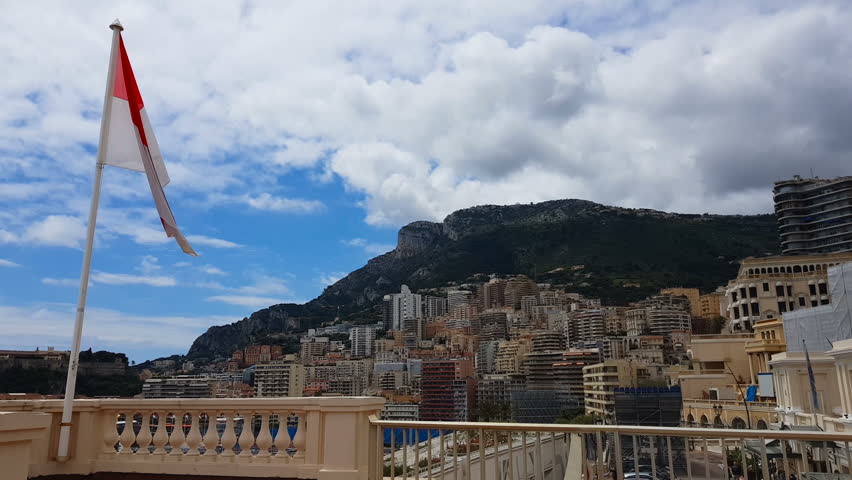 Flag of Monaco fluttering against background of mountain and resort cityscape