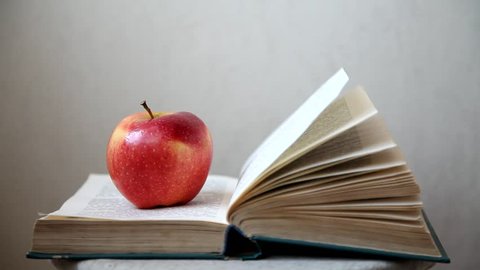 The red Apple is lying on an open book with moving pages