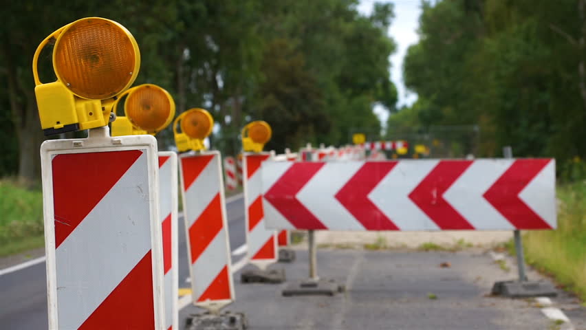 Road works with excavations marked with barriers and orange flashing warning lamps. Blocked street for traffic due to renovation. Royalty-Free Stock Footage #1020073306