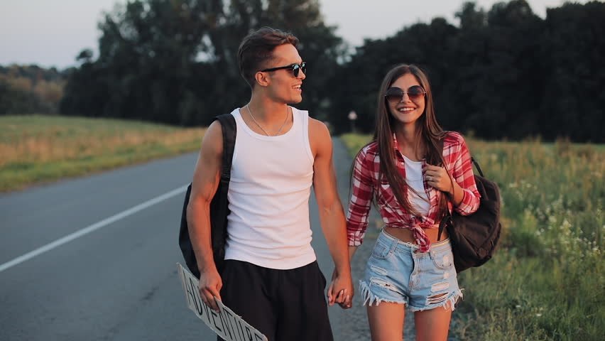 Couple On Vacation Hitchhiking Along Road and Holding Adventure Sign. Summer time. Hitchhiking, tourists, adventures concept