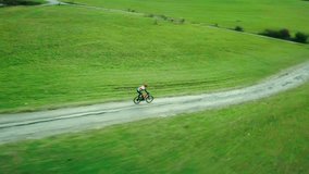 Aerial View bicyclist rides on a mountain road in summer sunny day around trees and mountains background under sun light, Drone 4K Video Aerial View
