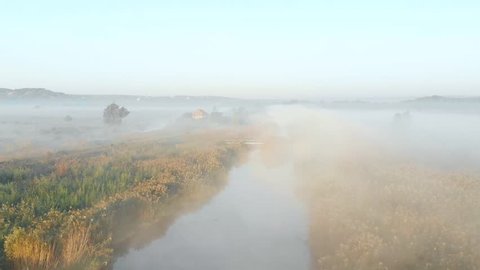 Shooting from the drone, flying over the misty river in the early morning