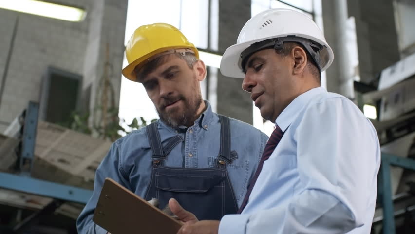 Low angled panning shot of middle aged Latin American manager in hardhat explaining something on clipboard and instructing bearded male worker in industrial plant | Shutterstock HD Video #1020085330