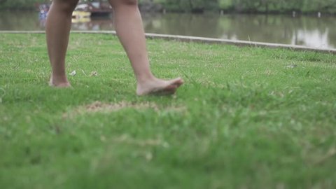 Female Barefoot Woman Legs Walking On A Green Grass Lawn On yard or next to water lake In super Slow Motion. Real life scene freedom concept feeling loose 