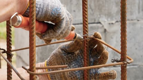 Close up hands builder in working dirty gloves tie the steel wire on the rebar with the help of a tool, creating a strong frame for reinforced concrete structures at the construction site of the house