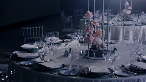 Camera rotates from right to left around a wedding decorated table with wedding bouquet in tall metall vase on dark background and rays of light beaming trough smoke or haze. 50mm wide open lens.