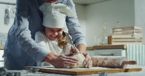 A mother has fun while showing how to cook to her daughter dressed as a chef in the kitchen. Concept: Lovo, holiday, family