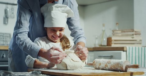 A mother has fun while showing how to cook to her daughter dressed as a chef in the kitchen. Concept: Love, holiday, family
