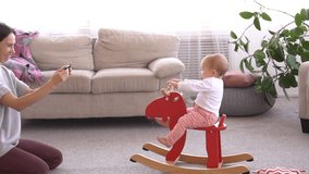 Mother photographing baby girl playing on rocking deer at home