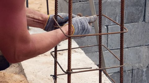 Close up hand builder working in dirty gloves, knotted steel wire for the fixations reinforcement, creating a frame for concrete structures on the construction site.