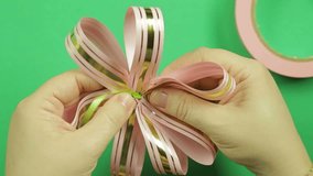 Female hands give shape to a pink ribbon bow on a green background