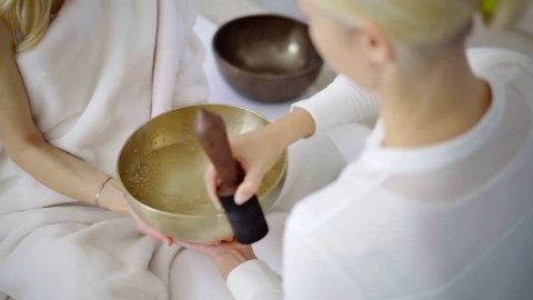 Shot from above of professional spa therapist playing a copper singing bowl for client, traditional tibetan therapy.