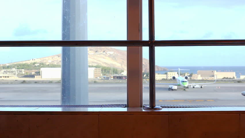 Man walking back and forth with carry on luggage at Las Palmas airport terminal. Airplane on landing area as passenger passes by. Travel, transportation concepts
