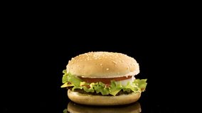 Rotation of delicious burger over black background. loop video, 4K