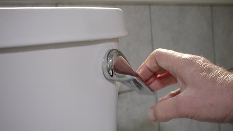 Slow motion close POV shot of a man's hand flushing a toilet.