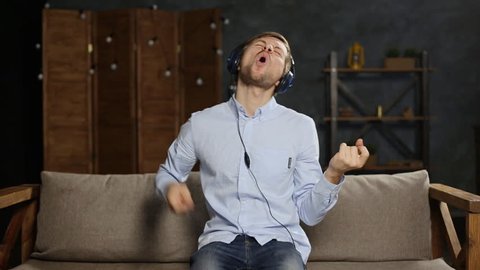 Young man in headphones listening to music and playing on invisible air guitar
