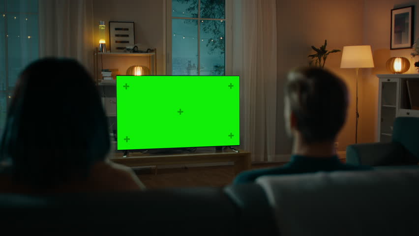 Couple Watches Green Mock-up Screen TV while Sitting on a Couch in the Living Room. Romantic Evening for Boyfriend and Girlfriend. | Shutterstock HD Video #1020144166