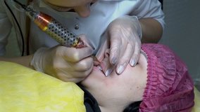 A young girl doing the procedure of permanent makeup lips in a beauty salon. Beautician needle pricks her paint on the lips. Close up. 4K. 25 fps