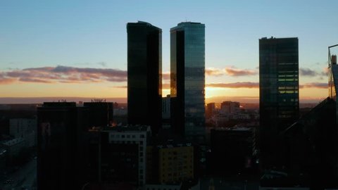 Highrise business district with sun looking into the camera (trademarks blurred). Aerial pan of setting sun peaking between the towering buildings on Maakri street in Tallinn