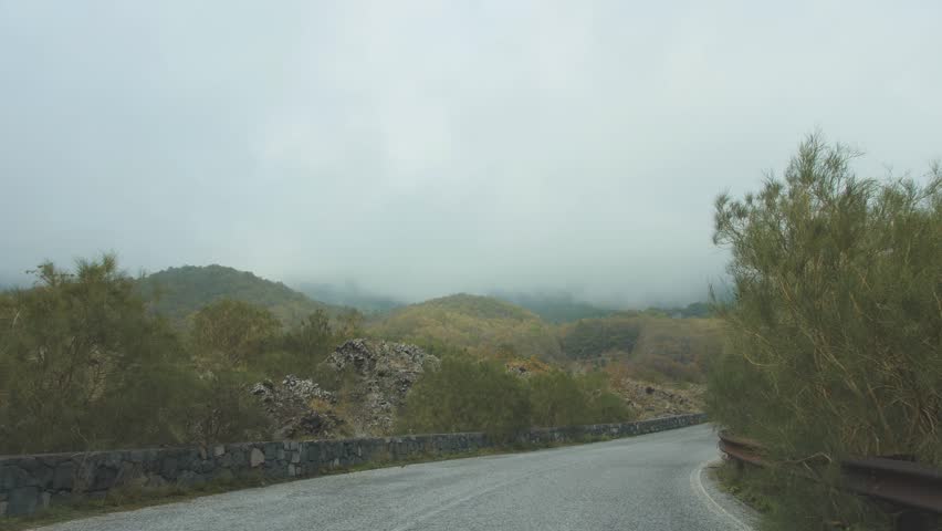 Driving along the winding road among mountains covered with clouds. POV shot