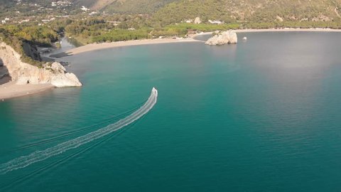 Motor boat floats towards river mouth at woody coastline. Aerial shot of sea shore. Campania, Italy