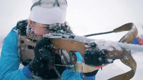 Sportswoman is shooting from her riffle during a biathlon race in a lying position