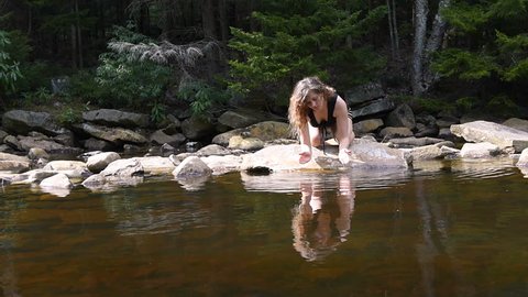 Young woman enjoying nature, forest on peaceful, calm Red Creek river in Dolly Sods, West Virginia during sunny day with reflection dipping hands in fresh, splashing water, drinking