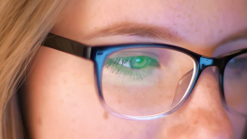 Close-up shooting caucasian woman is looking at screen reflected in her glasses, IT specialist, smart modern person
