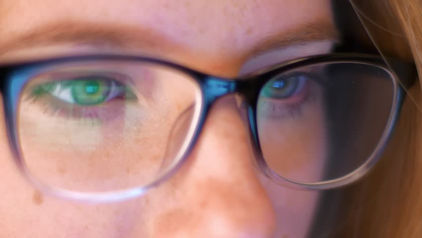 Close-up reflection of laptop screen in gleasses of caucaisna girl hacker, looking at copmuter, beautiful eyes of smart person indoor
