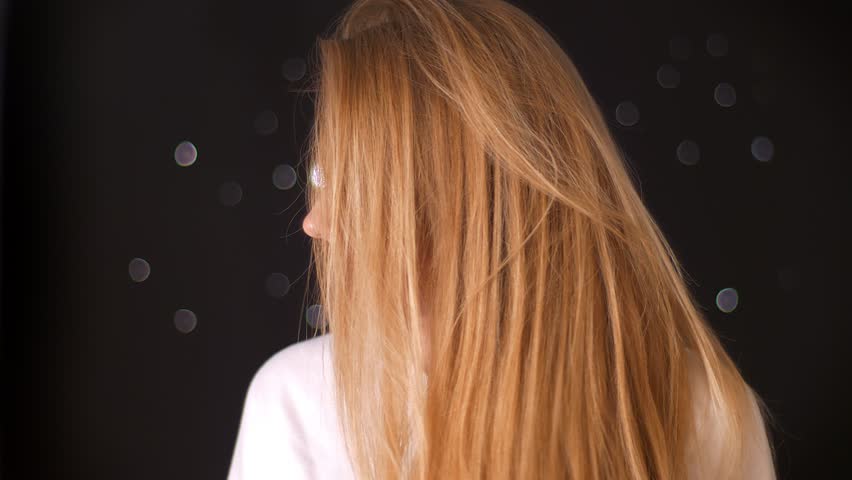 Relaxed happy blonde is turning her hair and moving while looking at camera in glasses and showing artistic happy emotions in black studio