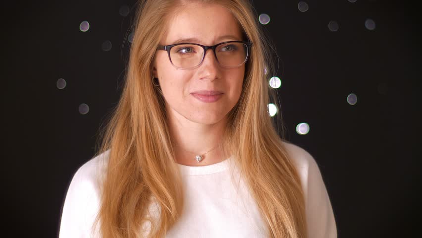 Awesome laughing caucasian female is standing relaxed and showing happiness and wearing glasses on dark background alone, moving, casual style