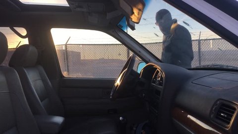 Car thief checks drivers door window before smashing glass in, entering, and then pounding screwdriver into ignition to start car; in angled sunset lighting.