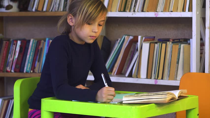 Little Girl learning lessons, cute girl making her homework, schoolgirl studing at home at the table, children