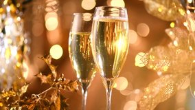 Holiday Champagne over Golden glow background. Christmas and New Year celebration. Two Flutes with Sparkling Champagne over Holiday gold Bokeh Blinking Background. Table setting, decoration. Slowmo