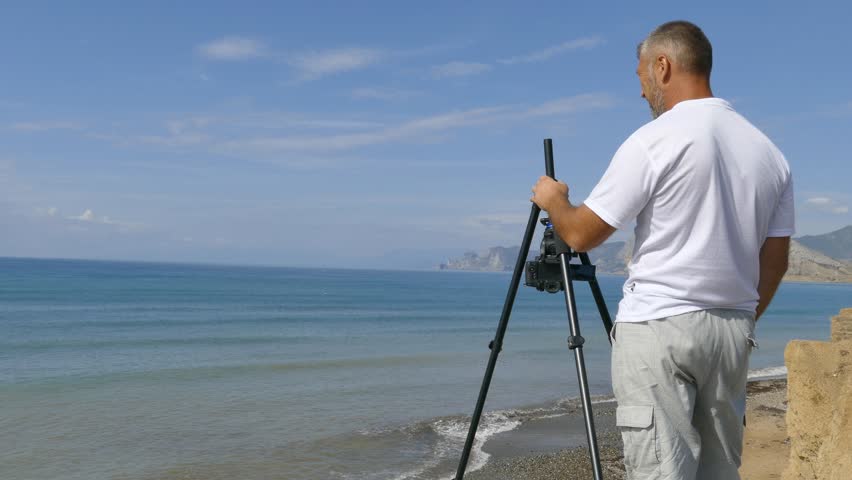 Videographer shoots the coast on a camera mounted on a tripod