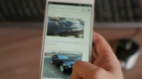 A man chooses to buy a car on the site. Looking at used vehicle to buy on a smartphone app. Close Up. Screen is blurred. 4K UHD. 