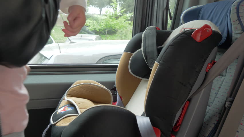 A caring mother puts her little daughter in a safe child seat of the vehicle.