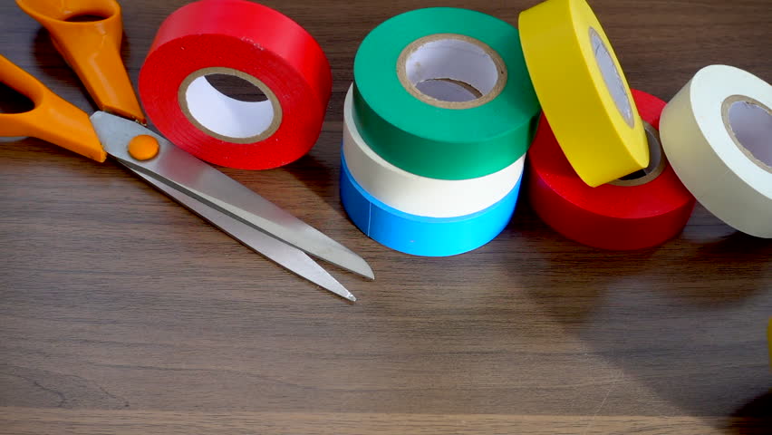 Slow motion close POV shot of a pair of scissors next to a pile of red, yellow, green, blue and white  electrical tape, with a few rolls slowing moving in front. Royalty-Free Stock Footage #1020187273