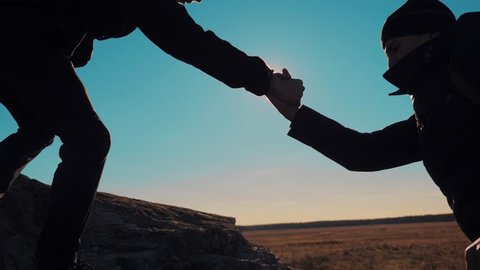 teamwork business travel trip. two men with backpacks hiking help each other silhouette in mountains with sunlight. slow motion video. teamwork friendship hiking help each other trust assistance the