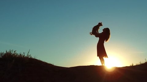 girl lifts a small dog at sunset silhouette. woman playing with a dog on nature. silute sunlight. friendship man and pet concept lifestyle