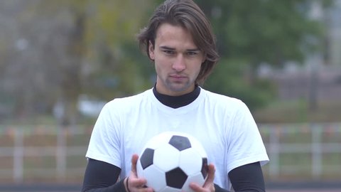 Portrait of a young guy in a sports t-shirt holding a soccer ball in his hands and strictly looking at the camera Sports guy with a ball in his hands with a cheeky look