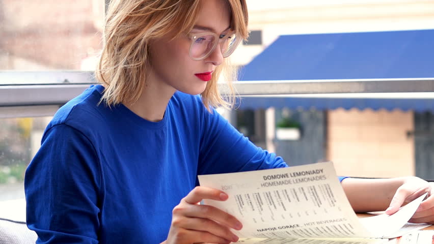 Young, beautiful woman reading menu in cafe in city, 4K

