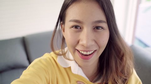 Asian blogger woman using smartphone recording vlog video in living room at home,female enjoy funny moment while lying on the sofa when relax at home. Lifestyle blogger making video at home.