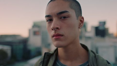 portrait attractive young mixed race man with shaved hair on rooftop at sunset wearing piercings looking confident in urban city background